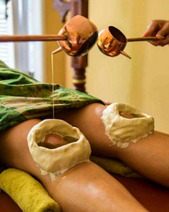 Picture of a healer pooring ayurvedic oil on Janu Basti treatment for healing join and knee pain